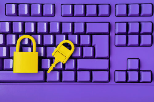 A yellow padlock and key rest on a purple keyboard